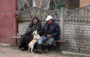 A dog near a man and a woman sitting on a bench in the village of Andriyivka, Bucha district