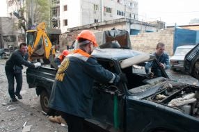Utility workers push a car damaged in the R-500 "Caliber" missile in Kharkiv