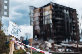 Caution with the inscription "Beware of mines" on the background of a ruined apartment building in Borodyanka