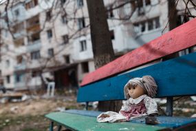 Doll on a bench on the background of a ruined apartment building in Borodyanka