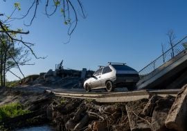 A car drives past a blown-up bridge