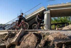 Cyclists pass by a blown up bridge
