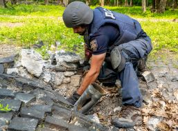 SES officer removes cluster munition remnants from fragment of Polish Memorial to Victims of Totalitarianism in Kharkiv