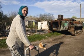 Elderly woman with a walker of the remains of military equipment of the Russian occupiers in the village of Sloboda