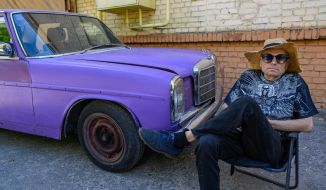 A man is sitting on a chair near the car