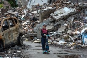 A boy on a scooter near the destroyed houses in Chernihiv