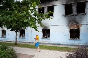 Женщина проходит возле разрушенного в результате обстрелов российских оккупантов жилого дома