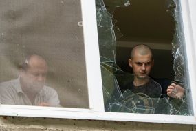 A man collects the fragments of a broken window in an apartment