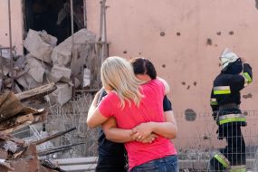 Women stand near the ruins of a destroyed house