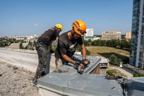 Будівельники знімають покрівельне залізо з даху пошкодженої будівлі