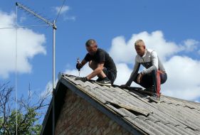 Men fix slate on the roof of a damaged residential building in the city of Bucha