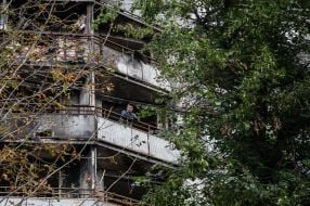 A man smokes on the balcony of a residential building destroyed by rocket fire