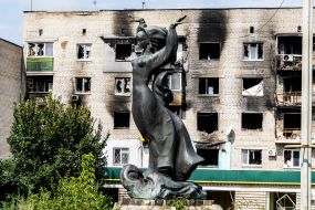 A statue of a woman against the background of a burnt residential building in the newly liberated city of Izyum