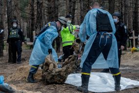Forensic experts pack an exhumed body into a bag at a mass burial site in a forest near the town of Izyum