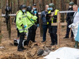 Forensic experts examine an exhumed body at the site of a mass burial in a forest near the town of Izyum