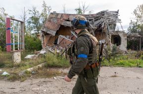 A soldier of the National Guard of Ukraine walks past a destroyed house in one of the villages