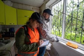 Volunteers measure the size of a window shattered by an explosion in a house damaged by a MLRS salvo