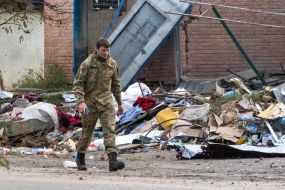 Український солдат іде повз зруйнований будинок