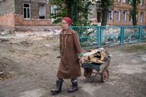 A volunteer feeds anAn elderly woman carries firewood
