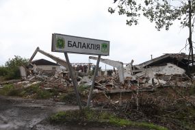 Road sign with the inscription "Balaklia" on the background of destroyed buildings
