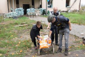 Volunteers help a local woman carry packages with humanitarian aid