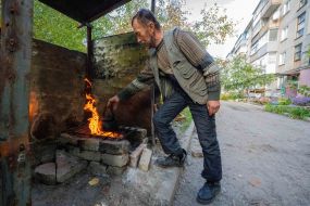 A local resident heats a kettle on a fire in front of the apartment building where he lives in the city of Kupyansk