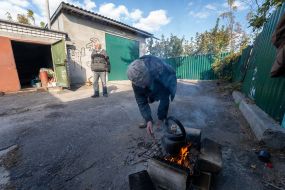 Local residents heat a kettle in front of the garage where they live in the city of Kupyansk