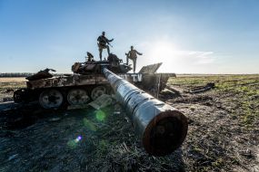 Ukrainian soldiers stand on a burnt Russian tank in a field