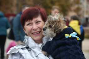 A woman is holding a dog with a yellow and blue bow