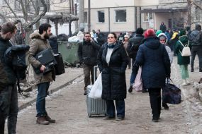 People are waiting near a house destroyed by rocket fire