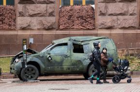 A woman with children walks by a damaged military vehicle on Khreshchatyk Street