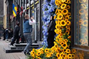 A man takes a picture of a woman near a shop window decorated with flowers
