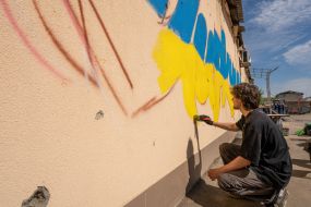 A young man writes the name of the village in the colors of the national flag of Ukraine