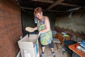 Местная жительница Ирина Хмель достает хлеб из ящика с гуманитарной помощью в своем разрушенном доме в Харьковской области