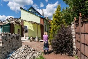 A woman watches as volunteers repair the roof of her destroyed house