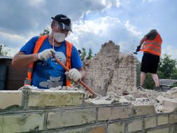 Volunteers clear broken bricks from the yard of one of the private houses destroyed by the Russian occupiers in the village of Gorenka