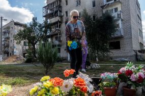 A woman lays flowers near a house destroyed by an aerial bomb dropped from a Russian plane