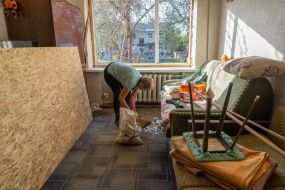 A woman sweeps the glass in her apartment in a building damaged by an aerial bomb explosion