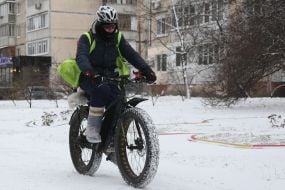 A courier on a bicycle walks along a snowy street in Kyiv