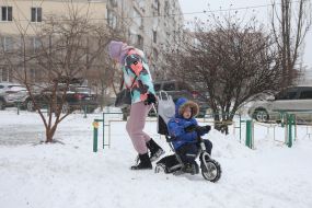 Жінка везе дитину на триколісному велосипеді засніженою вулицею