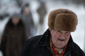 Літній чоловік в теплій хутряній шапці  на засніженій вулиці в Києві