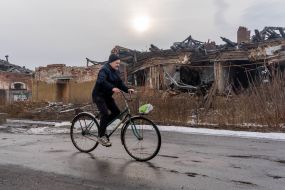 A man rides a bicycle against the background of a destroyed building in the city of Vovchansk