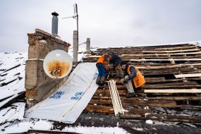 Utility workers restore the roof of a damaged house