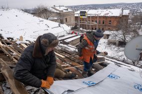 Utility workers restore the roof of a damaged house
