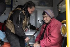 Волонтер сопровождает пожилую женщину во время эвакуации мирных жителей из районов боевых действий недалеко от города Волчанск