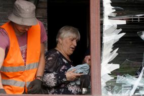 A utility worker helps a woman remove broken glass from her apartment window after a Russian UMPB D-30 projectile exploded in Kharkiv