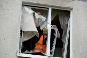 Employee of the communal service removes broken glass from the window of apartment after the explosion of a Russian UMPB D-30 projectile in Kharkiv