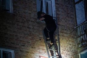 A man on a ladder near the window of an apartment building destroyed by a Russian missile in Kharkiv