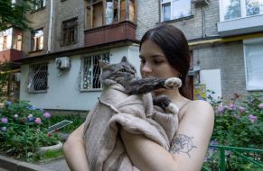 A woman with a cat in her arms near a destroyed residential building in Kharkiv
