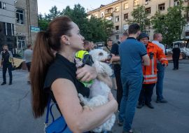 A woman with a dog in her arms near a destroyed residential building in Kharkiv
